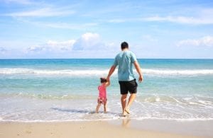 Man walking on beach holding young daughters hand