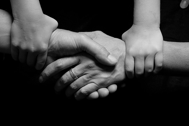 A black and white picture of two adults holding hands, while a child holds both of their wrists, holding them together.