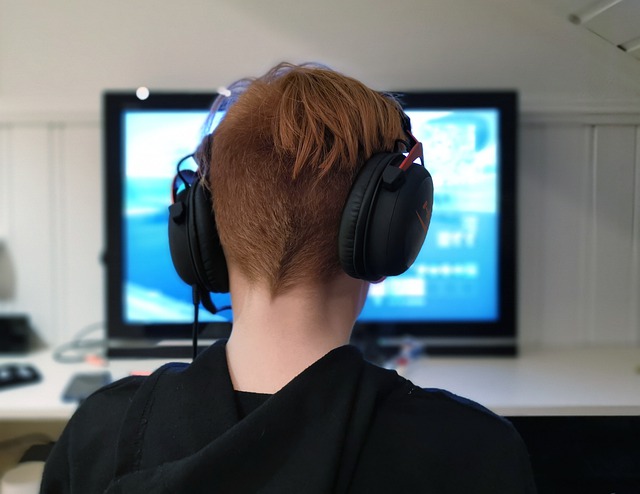 A picture of the back of a teenager's head - he's wearing gamer headphones and staring at a game on a computer screen.