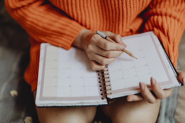 A woman's lap, with a date book open on it. She is checking the calendar and making notations on certain dates.