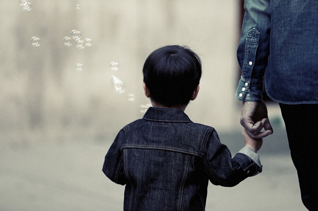 A picture of a little boy walking and blowing bubbles, while holding his parent's hand