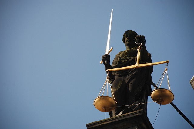 An upward angled picture of lady Justice, holding a golden scale and a golden sword.