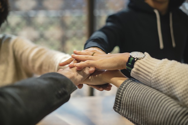 A group of people all placing their hands together in a circle, signifying working together and supporting one another.