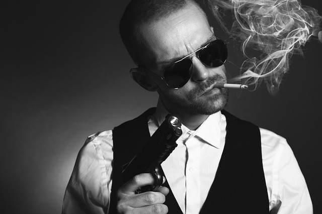 A black and white picture of a man smoking a cigarette and holding a gun up, as if he's about to rob you at gunpoint.
