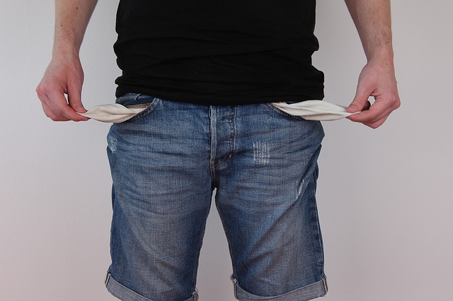 A man standing, pulling the insides of his pockets out to show that he has no more money.