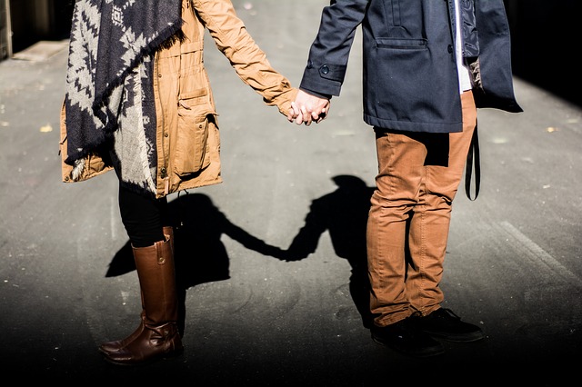 A man and a woman standing side by side by apart, holding hands but facing away from each other.