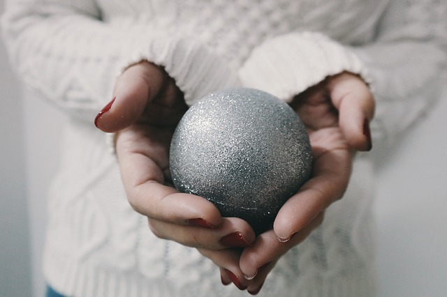 A close up of a woman's hands, holding a silver glitter Christmas tree ornament.