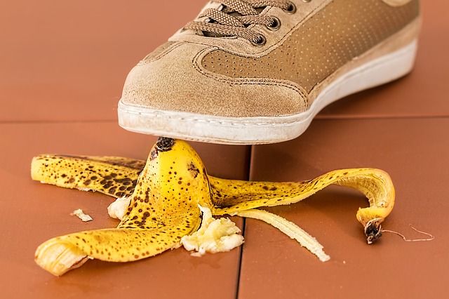 A person's foot, wearing a brown sneaker, about to step on a banana peel and slip.