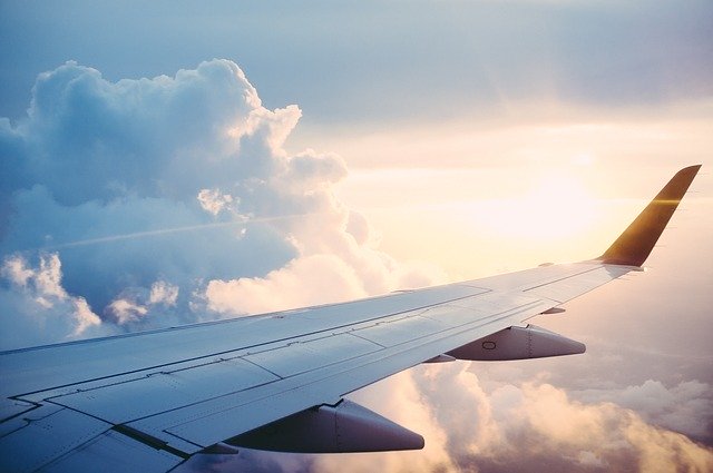 An airplane wing with a backdrop of sky and clouds with a sunrise in the distance.