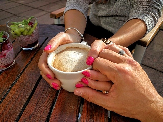 A couple at a table holding hands and drinking coffee.