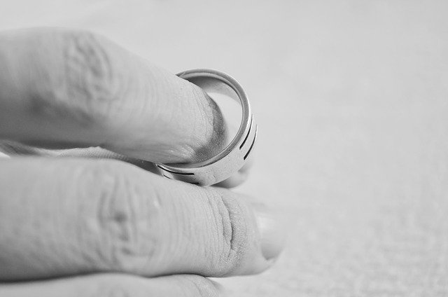 A person's fingers, as they slide their wedding ring off their finger.