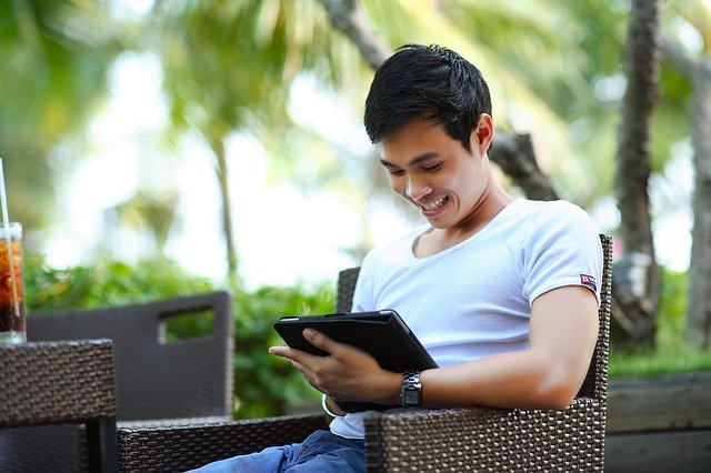 A man sitting and looking at a tablet screen, smiling happily.