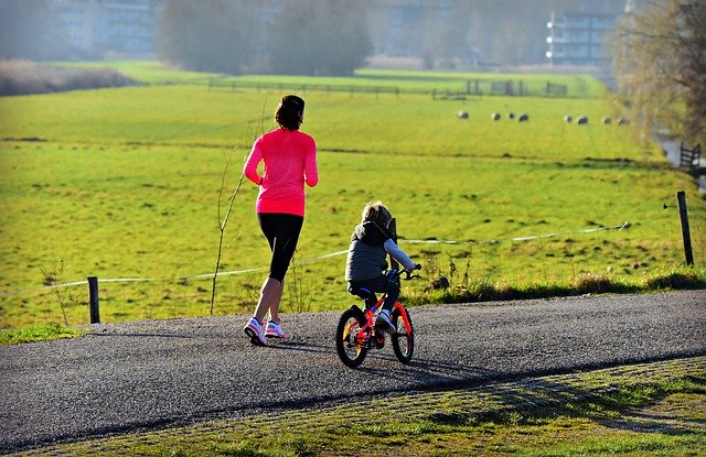 A woman and a child on the road together. The woman is running and the child is on a bicycle