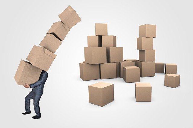A man carrying a large pile of boxes, with a pile of boxes in the background. A person preparing to move out.