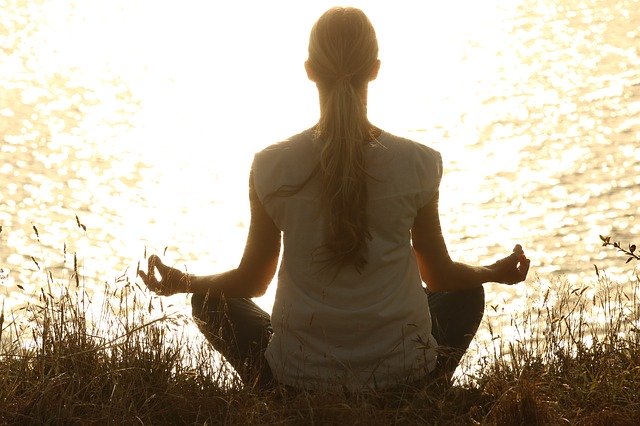 A silhouette of a woman meditating next to a lake, trying to stay calm during her divorce
