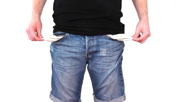 A man standing and pulling the insides of his pockets out to show that he has no money.