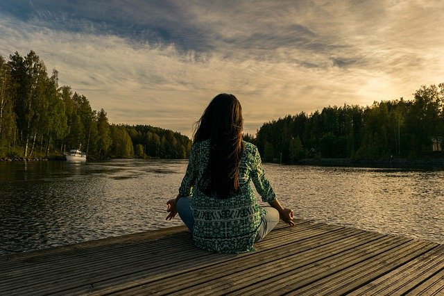 Woman sitting on a deck overlooking a lake, relaxing by doing yoga.