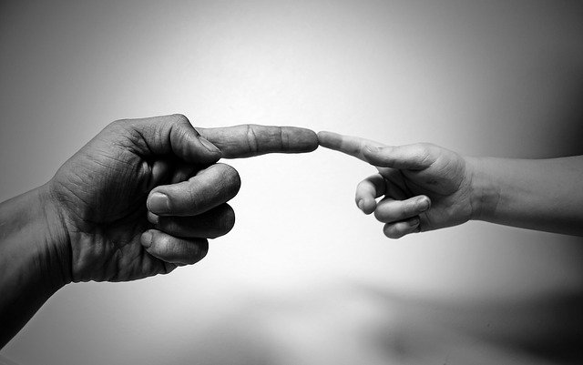 An adults' hand reaching out, and touching a child's fingertip with one finger, similar to Michelangelo's famous painting of God and Adam.