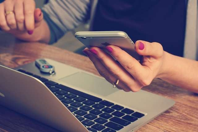 A woman sitting at a desk with a laptop and a smart phone, using an app to make co-parenting easier.