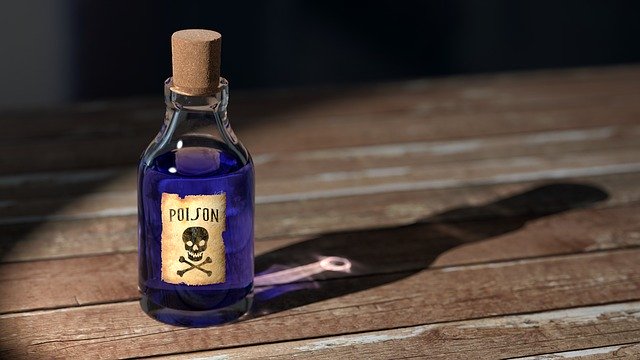 A bottle of purple poison, labelled "poison" with a skull and crossbones, sitting on an old wooden table.