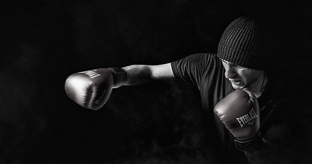 A black and white picture of a man wearing boxing gloves and throwing punches.