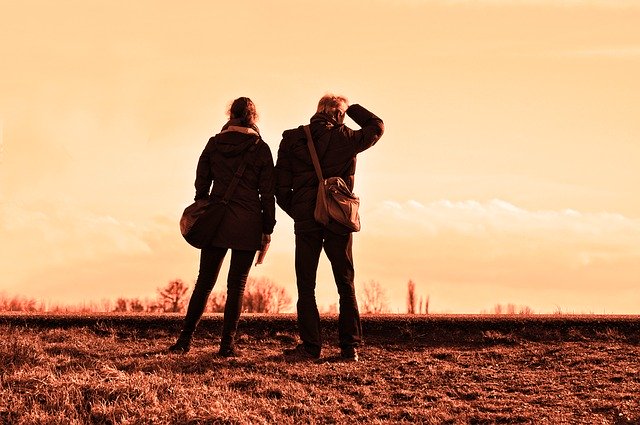 A sepia-toned image of a couple standing together with their travelling gear, but not holding hands and looking in different directions.