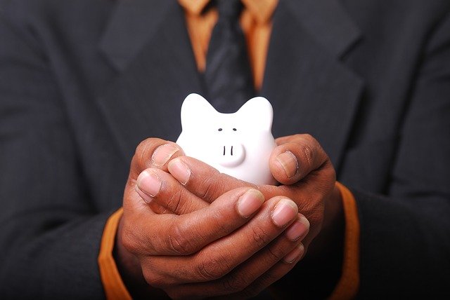 A lose up of a man in a business suit holding a small piggy bank in his hands, as if he only has a little money to offer.