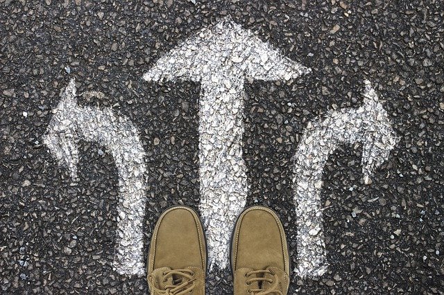 A pair of shoes, standing on a road in front of three arrows pointing in different directions
