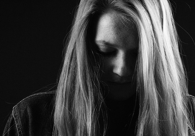 A close up black and white picture of a woman's face. She is looking sad, with downcast eyes.