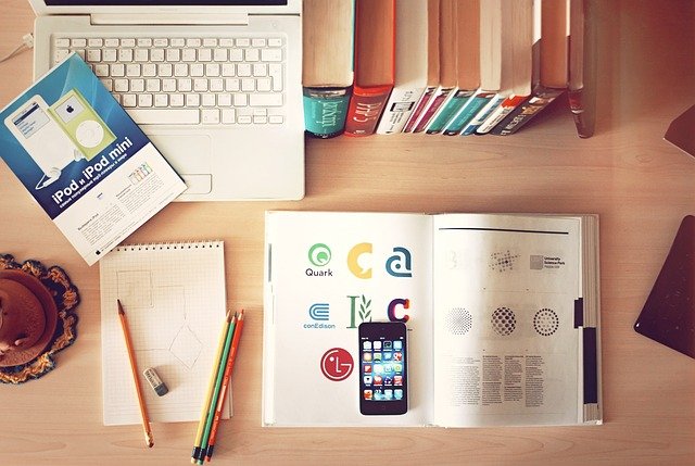  birds eye view of a school desk containing a lap top, books, pencils, a notepad, and a cell phone.