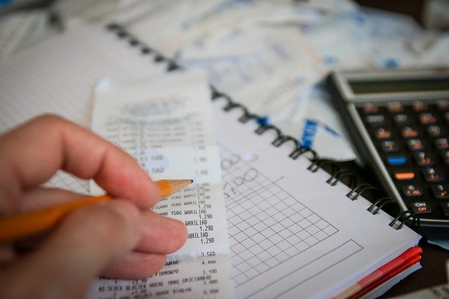 A person holding a pencil and adding up numbers on a receipt for tax purposes. There is a calculator and a stack of papers nearby.