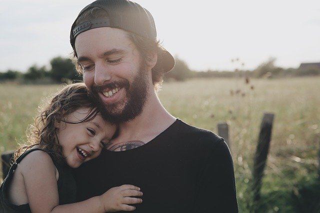 A young father smiling while he holds his young daughter in a hug.