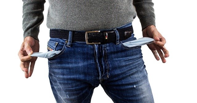 A man holding the inside of his pockets out to show that he has nothing in his pockets. But he may be hiding his money somewhere else.