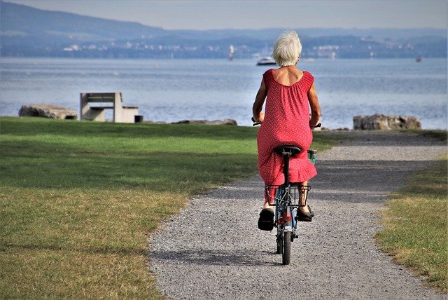 An older woman with grey hair riding a bicycle alone in the park.
