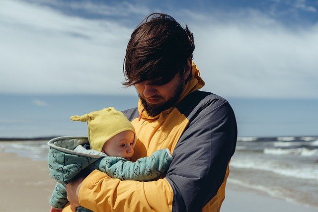 A young dad holding his baby at the beach.