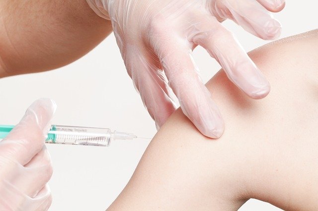 A close up of someone with gloves on pinching a child's arm and preparing to insert a needle to vaccinate them.