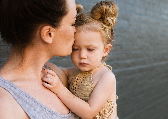 A young mom kissing her little daughter on the forehead.